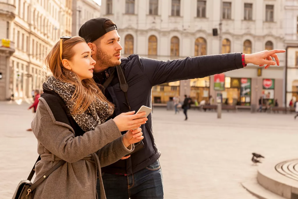 Man pointing and giving directions to American woman in European plaza. 